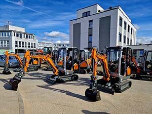 Mehrere Minibagger sind vor einem Gebäude abgestellt.