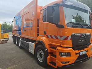 Ein großer orangefarbener Saugwagen steht vor einem Gebäude geparkt.