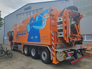 Ein großer orangefarbener Saugwagen ist vor einem Gebäude abgestellt.