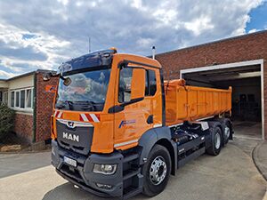 Ein Containerfahrzeug in orange steht vor einer Garage.
