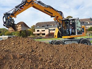 Ein großer Erdhaufen wird durch einen Bagger auf der Baustelle bewegt.