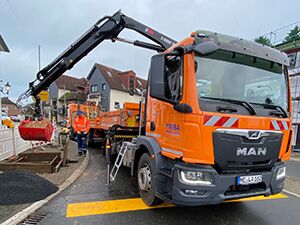 Ein großer orangefarbener Kranwagen steht auf der Baustelle und wird durch einen Mitarbeiter bedient.