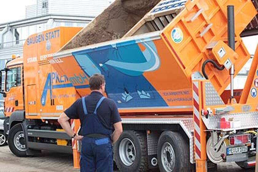 Ein großer orangefarbener Saugwagen von der Seite beim entleeren.
